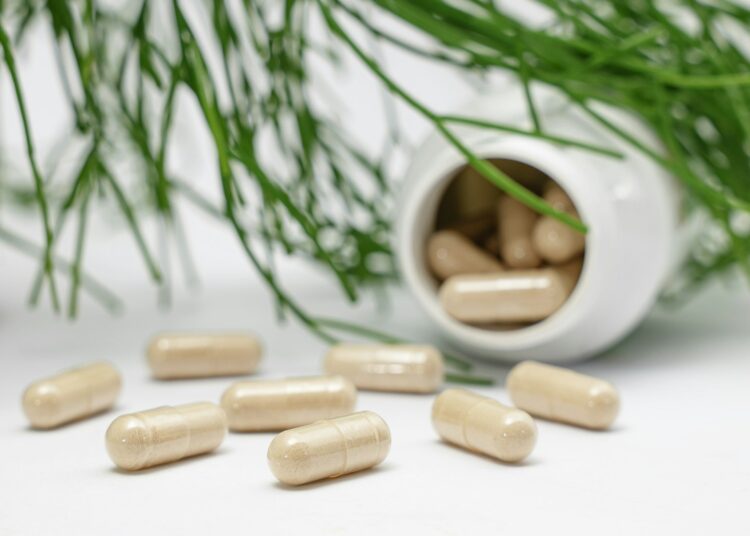 Potje met vitamine D-capsules naast een glas water op tafel