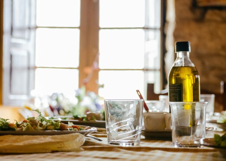Fles olijfolie van donker glas naast een schaaltje olie en groene olijven
