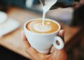 Kop koffie waarin een scheut romige creamer wordt geschonken