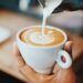 Kop koffie waarin een scheut romige creamer wordt geschonken