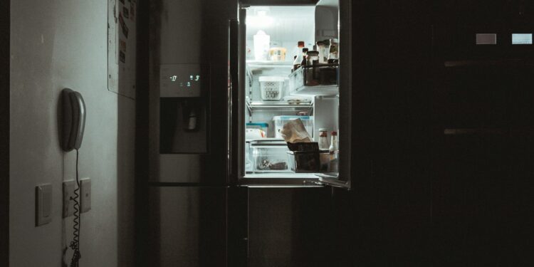 Iemand pakt 's avonds laat iets te eten uit een verlichte koelkast