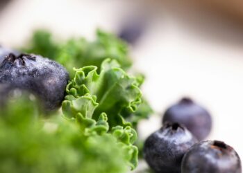 Een kom met blauwe bessen, noten en bladgroente op een houten tafel