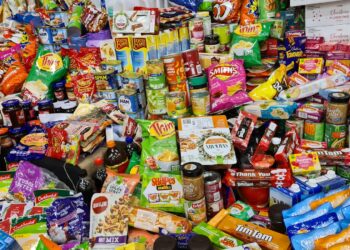 Verpakte snacks en frisdrank naast een bord met verse groente