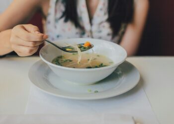 Vrouw proeft met een lepel van een pan soep op het fornuis