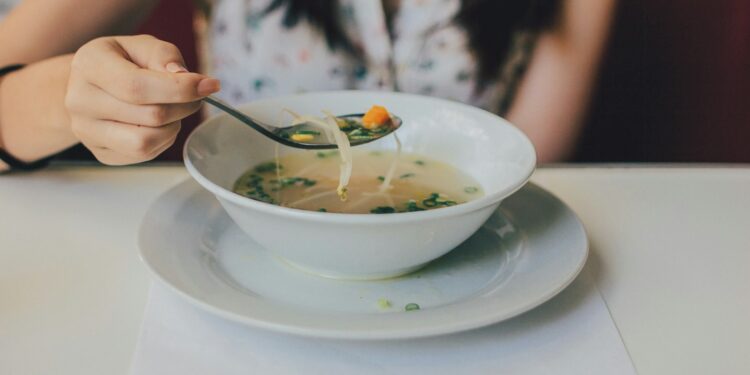 Vrouw proeft met een lepel van een pan soep op het fornuis