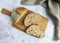 Gesneden zuurdesembrood naast een volkorenbrood op een houten plank