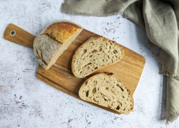 Gesneden zuurdesembrood naast een volkorenbrood op een houten plank