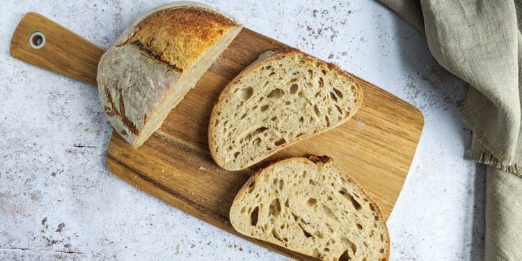 Gesneden zuurdesembrood naast een volkorenbrood op een houten plank