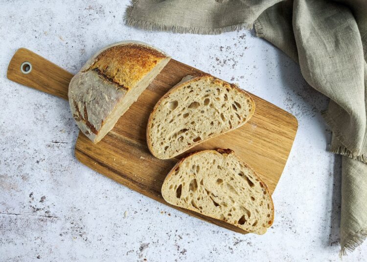 Gesneden zuurdesembrood naast een volkorenbrood op een houten plank